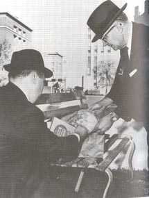 Figure 26. Press photo of bench with lunch bags being examined by two plainclothes officers