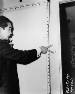 Photograph of Los Angeles Coroner Thomas Noguchi pointing to two bullet holes in doorfram